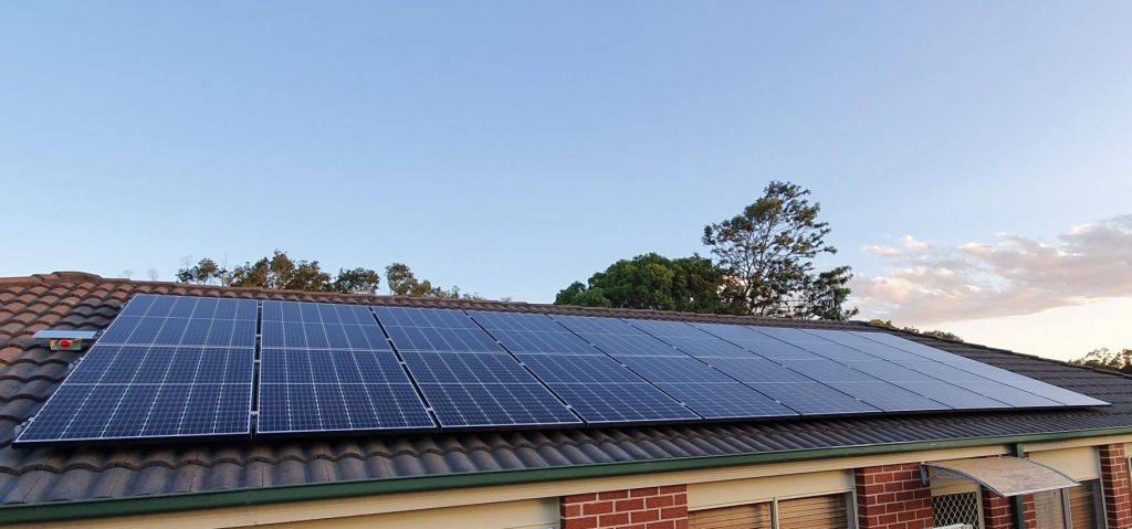 Row of solar panels across a dark tiled roof on a brick home
