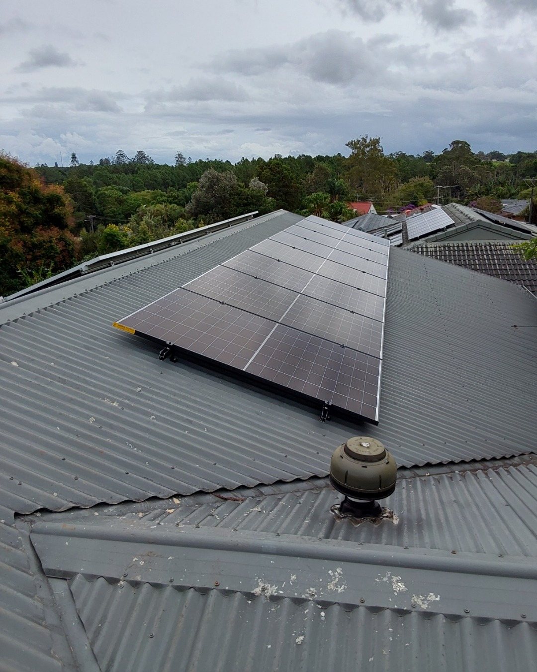 AIKO solar panels on a grey Colorbond roof with trees behind in Alstonville AIKO solar panels on a grey Colorbond roof with trees behind in Alstonville, part of a solar and 16 kWh Sigenergy battery install by Sun Connect Solar