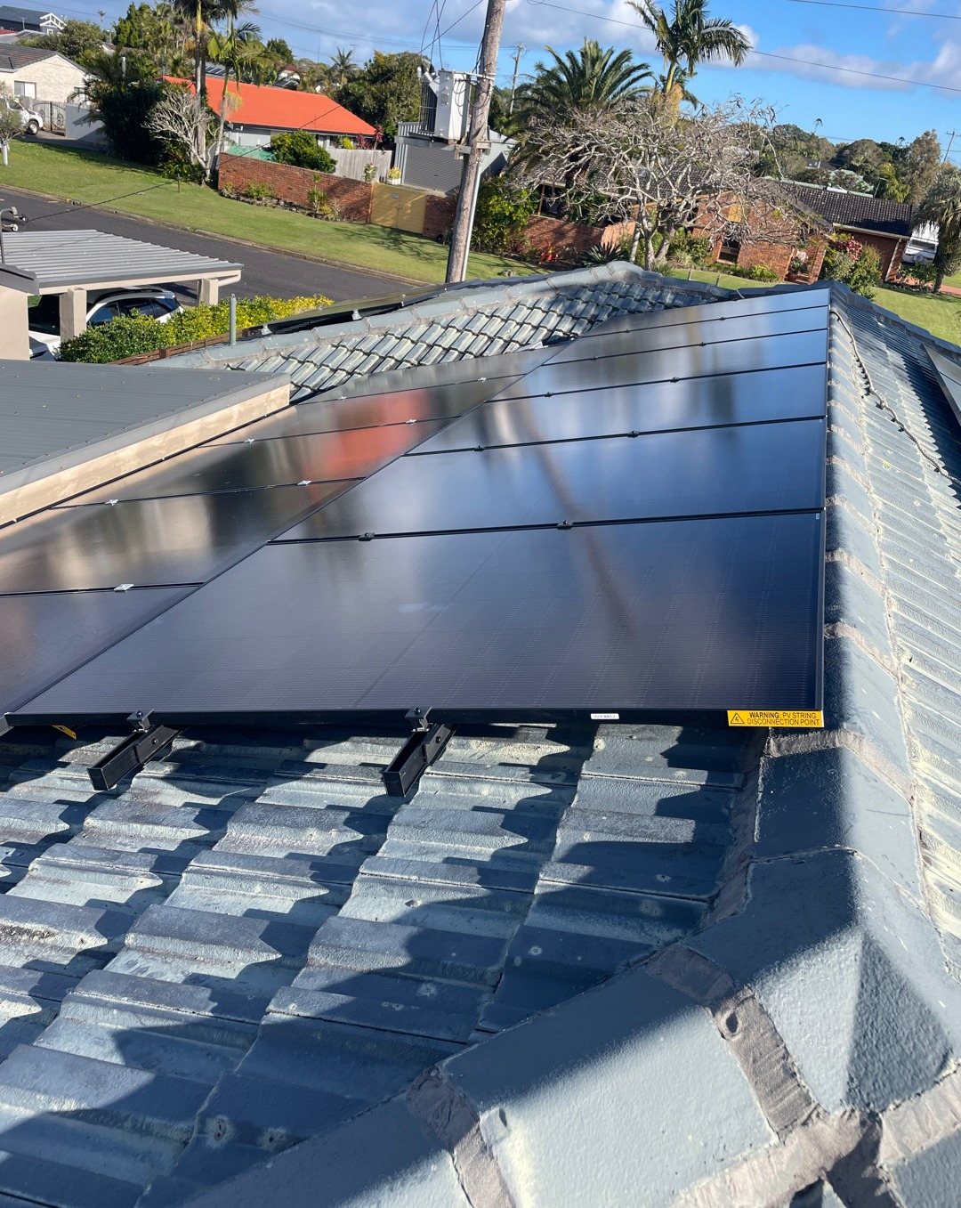 Jinko solar array on a tiled roof looking over a Ballina street with palms and brick homes, installed by Sun Connect Solar