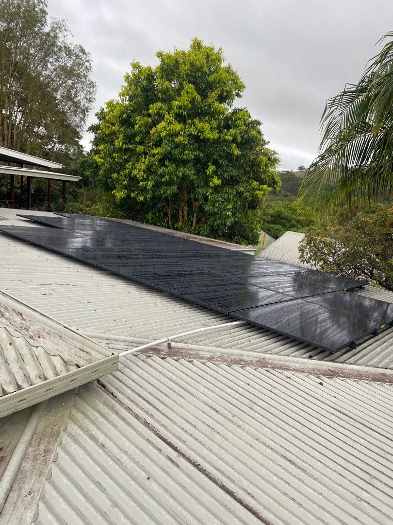 All-black AIKO solar panels along a metal roof with trees and the hills around Bangalow behind, installed by Sun Connect Solar