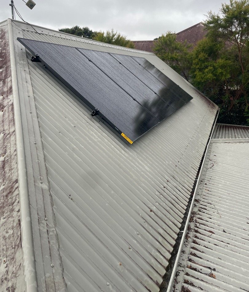 A block of all-black AIKO solar panels on a metal roof face among trees in Bangalow, installed by Sun Connect Solar