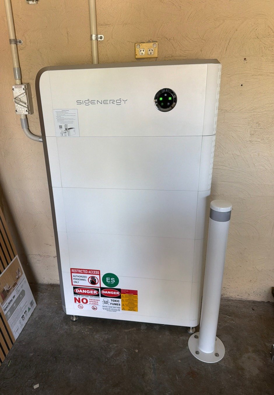 Sigenergy SigenStor battery with four modules Sigenergy SigenStor battery with four modules, about 32 kWh, and a protective bollard against a rendered wall in East Ballina, installed by Sun Connect Solar