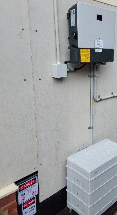 Sungrow hybrid inverter on the wall above a Sungrow SBR 9.6 kWh battery stack on gravel beside a weatherboard home in East Lismore, installed by Sun Connect Solar