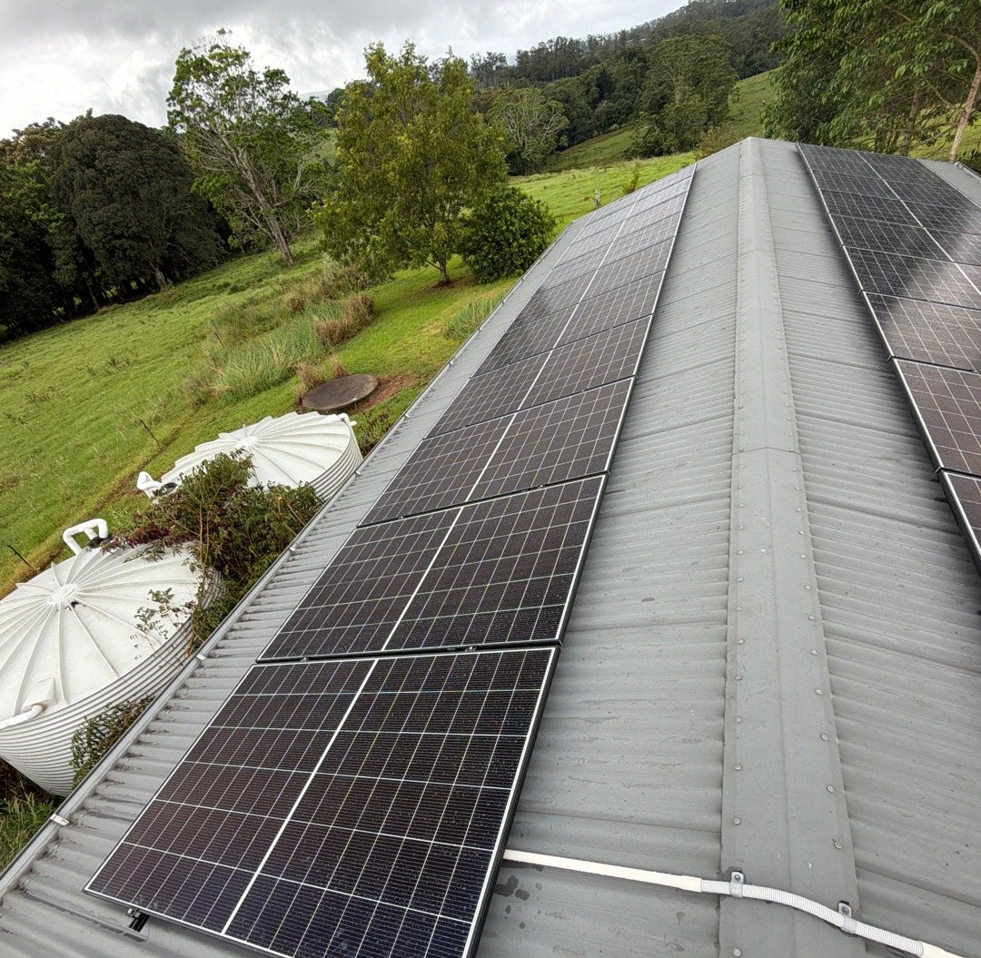 Two long rows of Trina solar panels along a shed roof beside water tanks and farmland at Eureka Two long rows of Trina solar panels along a shed roof beside water tanks and farmland at Eureka, installed by Sun Connect Solar
