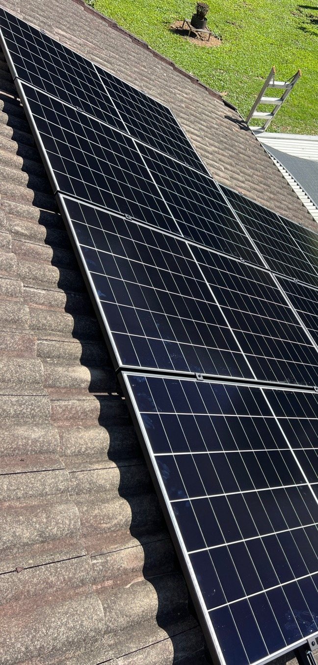 AIKO solar panels in rows on a tiled roof above a green hillside lawn at Federal AIKO solar panels in rows on a tiled roof above a green hillside lawn at Federal, near Bangalow, installed by Sun Connect Solar