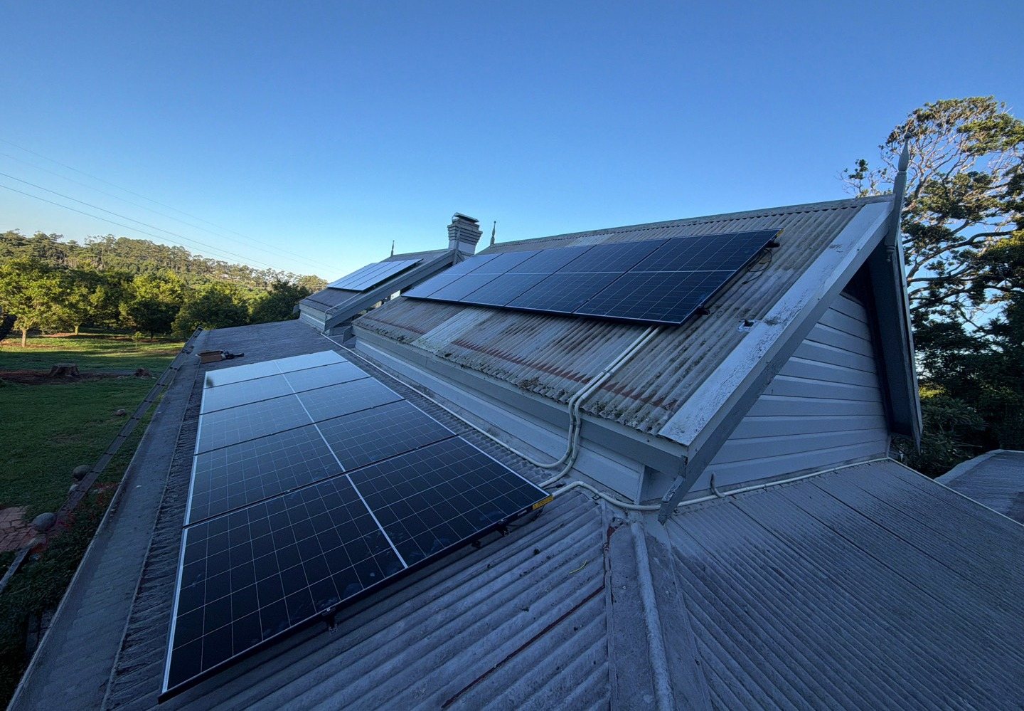AIKO solar panels on two faces of an old corrugated roof with an orchard and the hills around Federal behind AIKO solar panels on two faces of an old corrugated roof with an orchard and the hills around Federal behind, installed by Sun Connect Solar