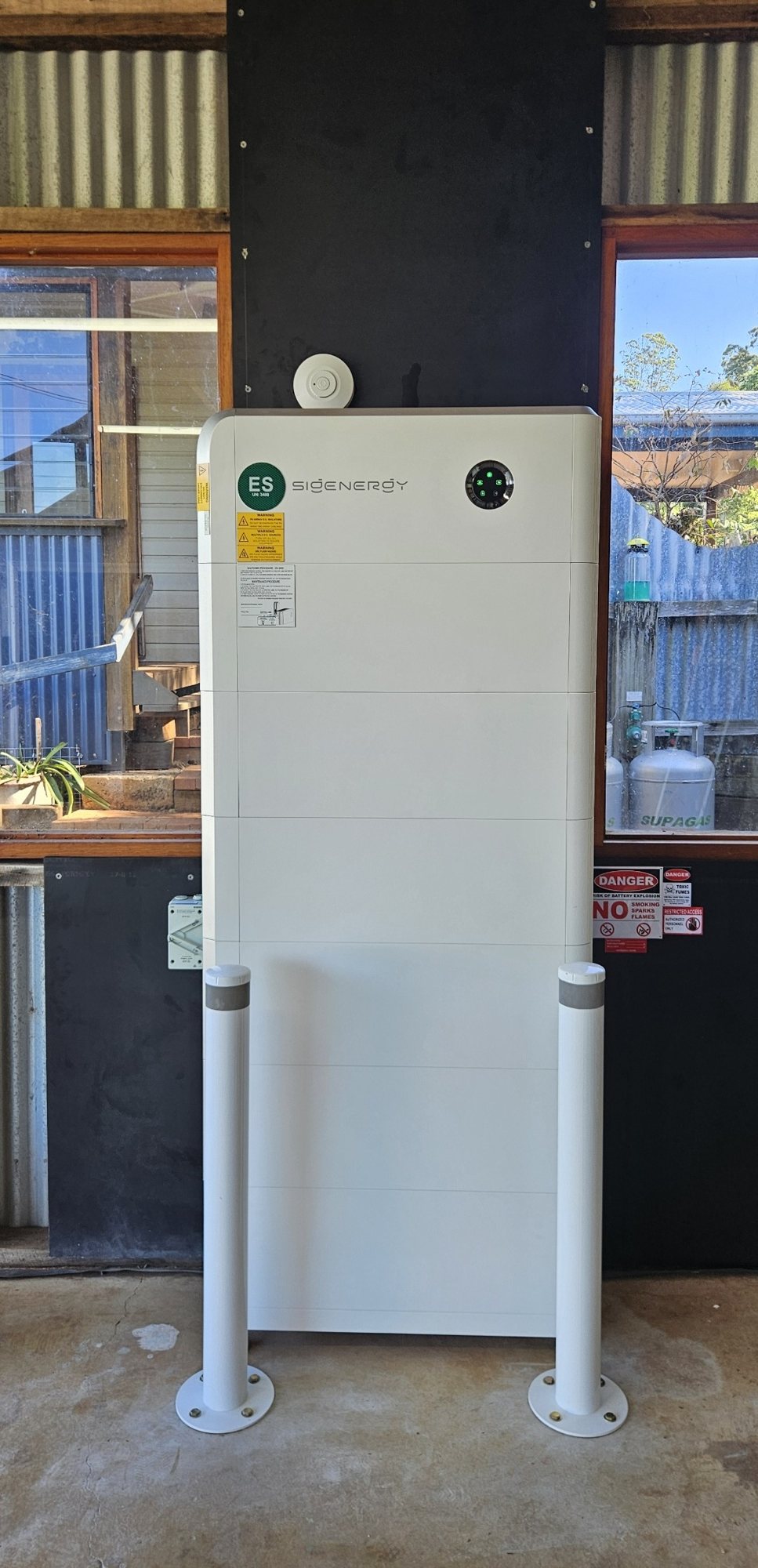 Tall Sigenergy SigenStor battery stack with six modules Tall Sigenergy SigenStor battery stack with six modules, about 48 kWh, between two protective bollards in a workshop at Federal, installed by Sun Connect Solar
