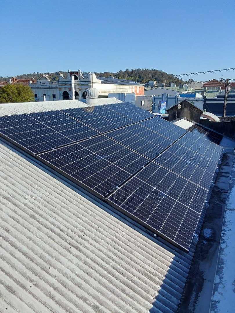 A Jinko solar array on a corrugated roof with heritage shopfronts and the hills of Lismore behind A Jinko solar array on a corrugated roof with heritage shopfronts and the hills of Lismore behind, installed by Sun Connect Solar
