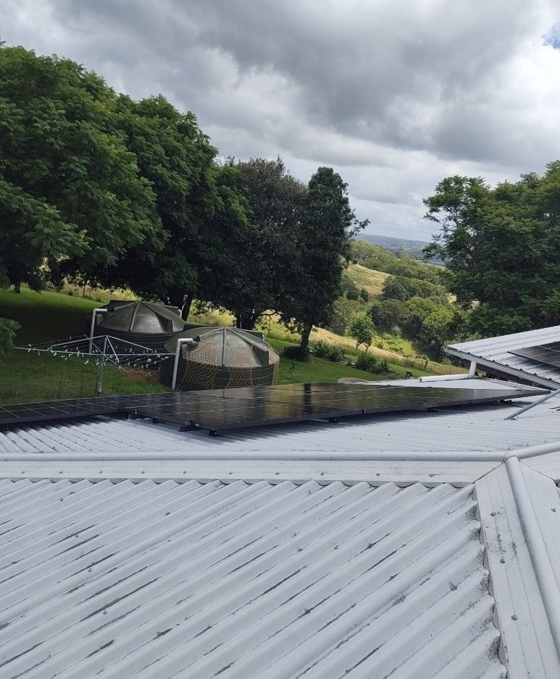 AIKO solar array on a corrugated roof with water tanks and rolling hills behind, Lismore hinterland, installed by Sun Connect Solar