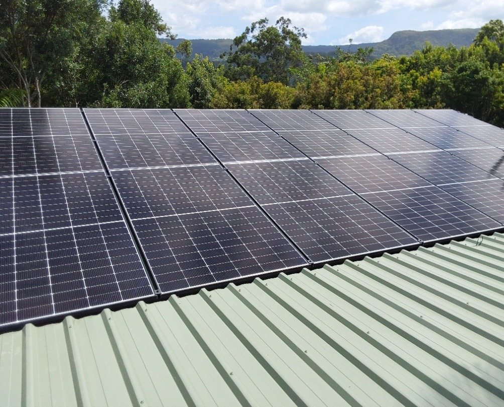 Jinko Tiger Neo solar panels on a pale green metal roof at Main Arm Jinko Tiger Neo solar panels on a pale green metal roof at Main Arm, with rainforest and the ranges behind, installed by Sun Connect Solar