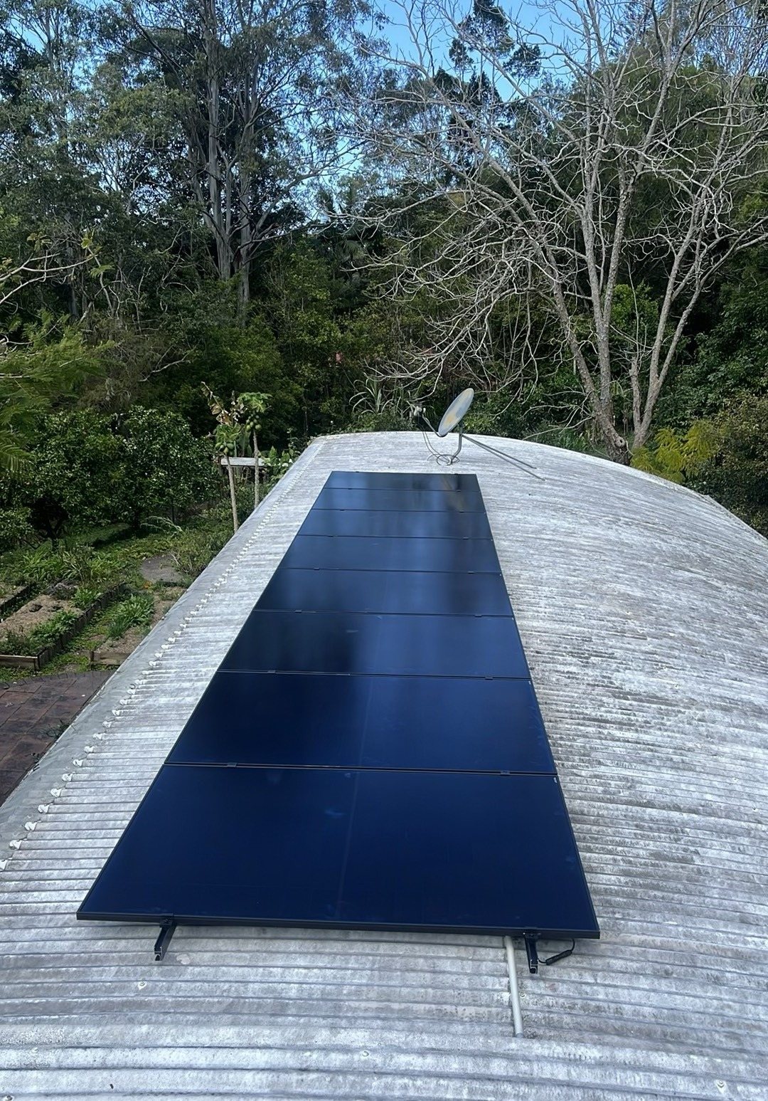 All-black AIKO solar panels on a curved corrugated roof surrounded by trees at Mullumbimby Creek All-black AIKO solar panels on a curved corrugated roof surrounded by trees at Mullumbimby Creek, installed by Sun Connect Solar