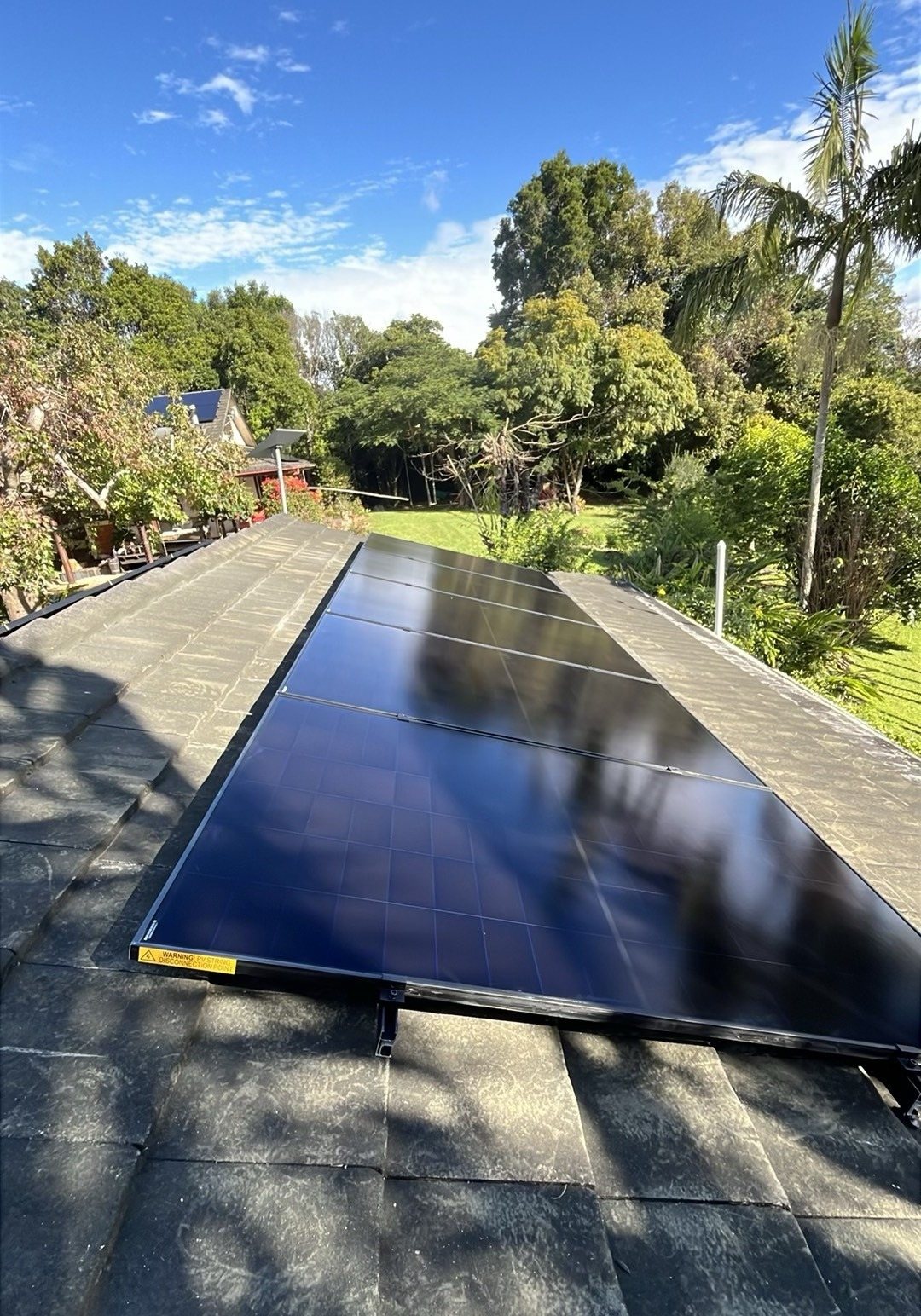 A long run of all-black AIKO solar panels down a tile roof among garden trees near Mullumbimby, installed by Sun Connect Solar