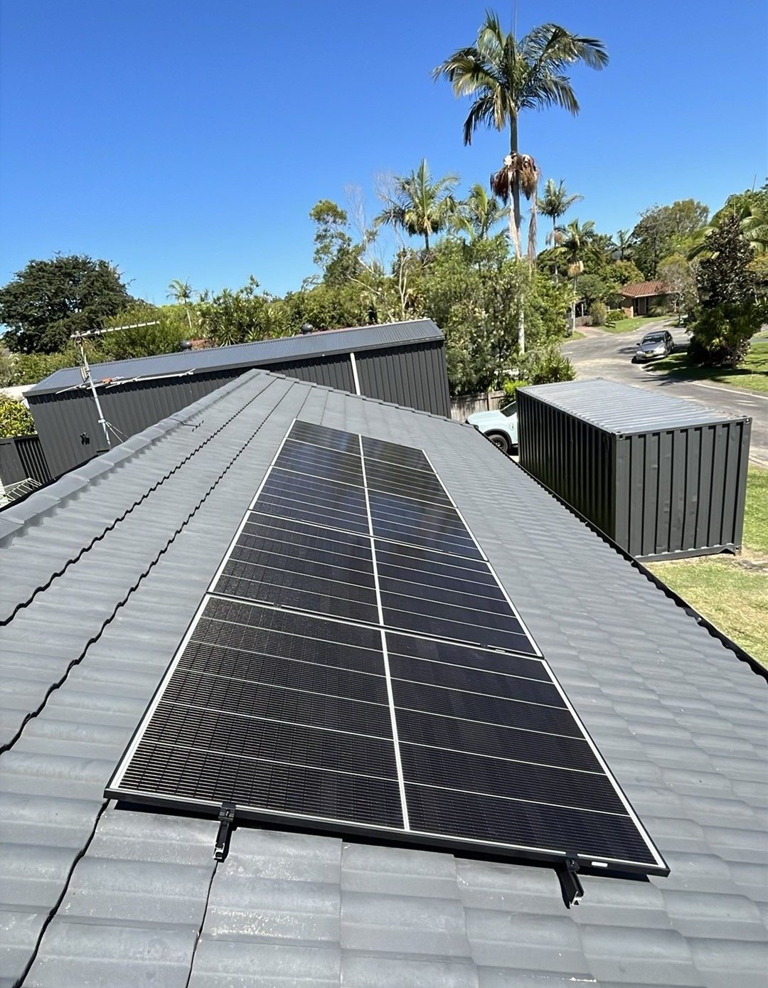 Jinko Tiger Neo III solar panels in a long block on a grey tile roof in Mullumbimby Jinko Tiger Neo III solar panels in a long block on a grey tile roof in Mullumbimby, with palms behind, part of a GoodWe battery install by Sun Connect Solar