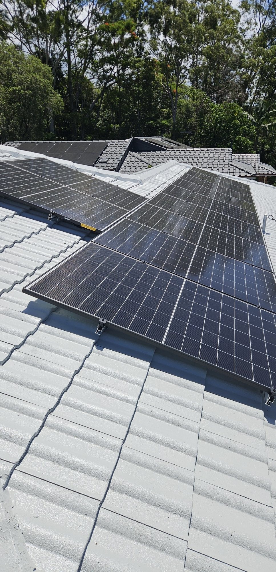 Rows of Jinko solar panels across the faces of a white tile hip roof among gum trees in Ocean Shores Rows of Jinko solar panels across the faces of a white tile hip roof among gum trees in Ocean Shores, installed by Sun Connect Solar