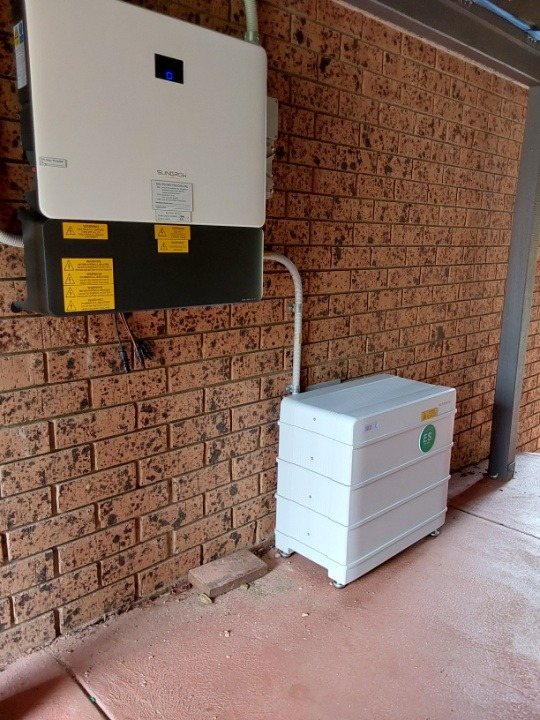 Sungrow hybrid inverter and SBR 9.6 kWh battery against a brick wall under a carport in Ocean Shores, installed by Sun Connect Solar