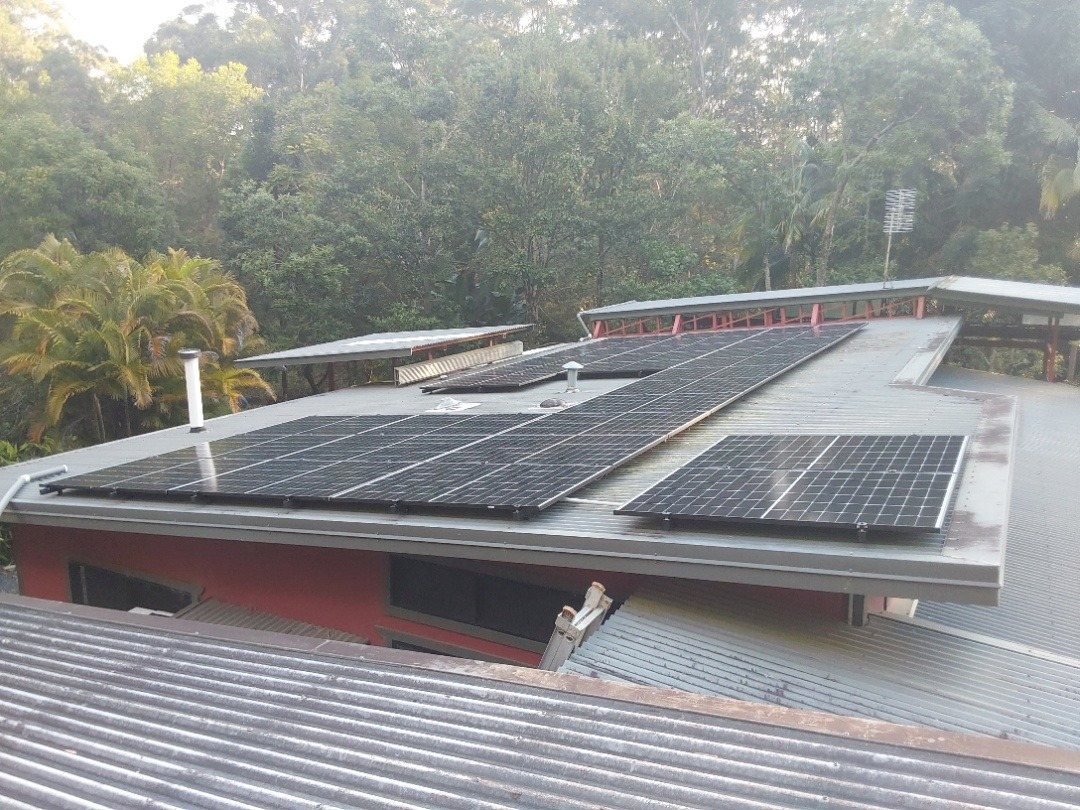 Jinko solar panels in rows on a low metal roof surrounded by rainforest at Rosebank Jinko solar panels in rows on a low metal roof surrounded by rainforest at Rosebank, installed by Sun Connect Solar