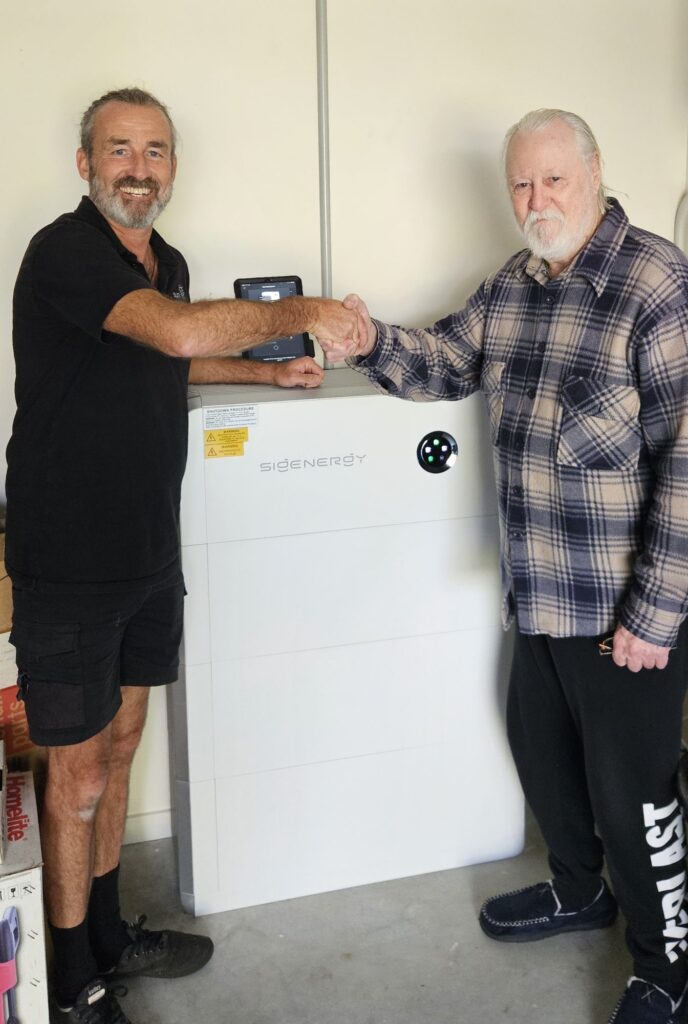 Customer shaking hands with a Sun Connect Solar electrician beside a new 24 kWh Sigenergy battery in an Ocean Shores garage