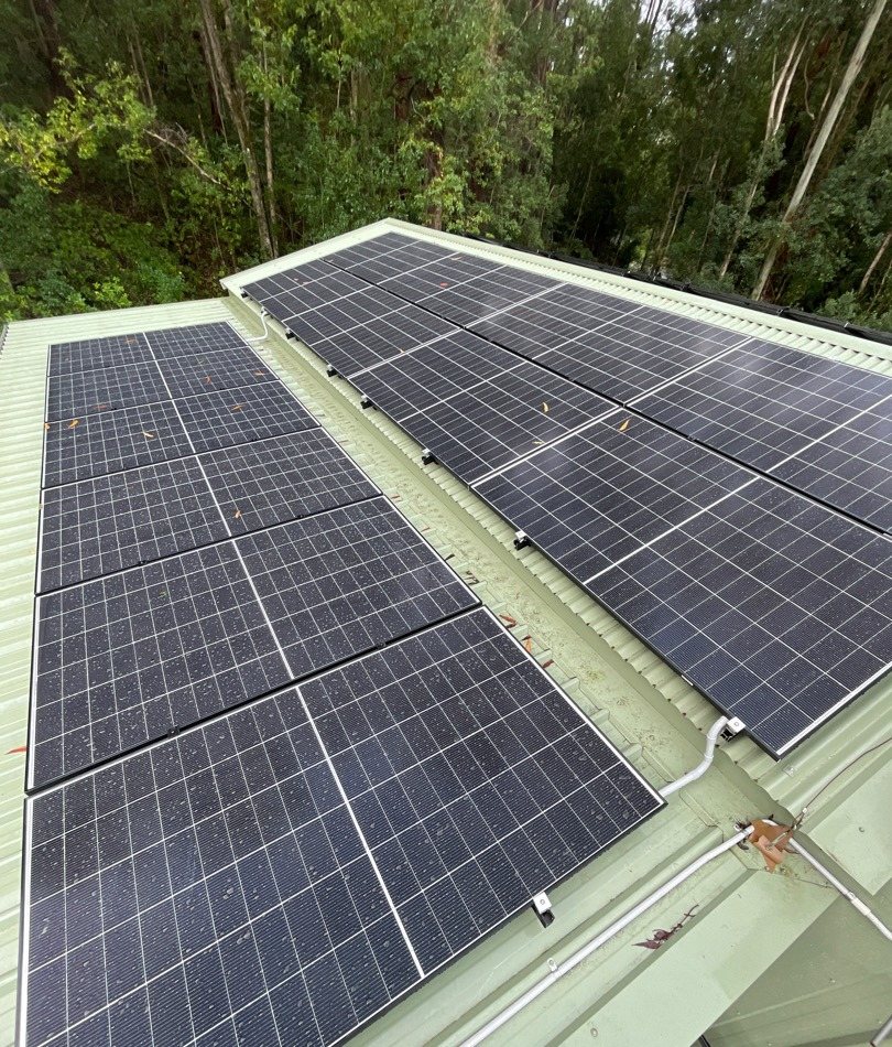 Part of a 23.46 kW Jinko solar array on Colorbond roofing with rainforest behind at Stokers Siding Part of a 23.46 kW Jinko solar array on Colorbond roofing with rainforest behind at Stokers Siding, installed by Sun Connect Solar