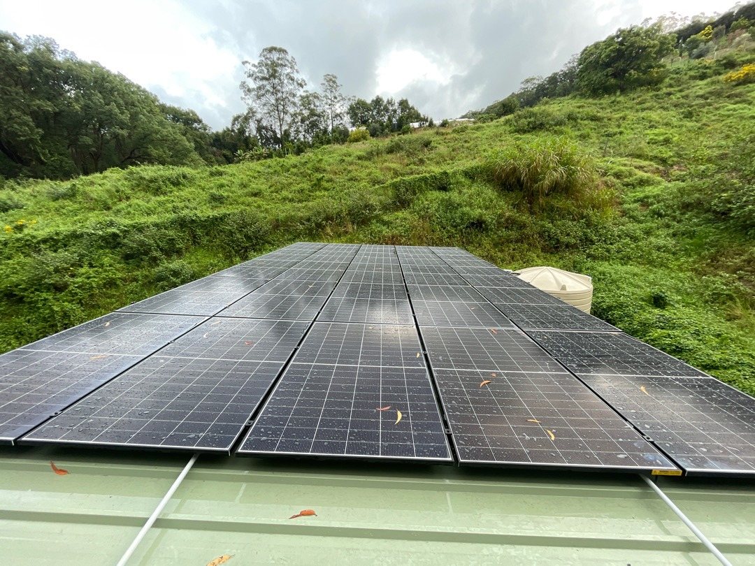 Jinko Tiger Neo solar panels on a pale green Colorbond shed roof below a grassy hillside at Stokers Siding in the Tweed Valley Jinko Tiger Neo solar panels on a pale green Colorbond shed roof below a grassy hillside at Stokers Siding in the Tweed Valley, installed by Sun Connect Solar
