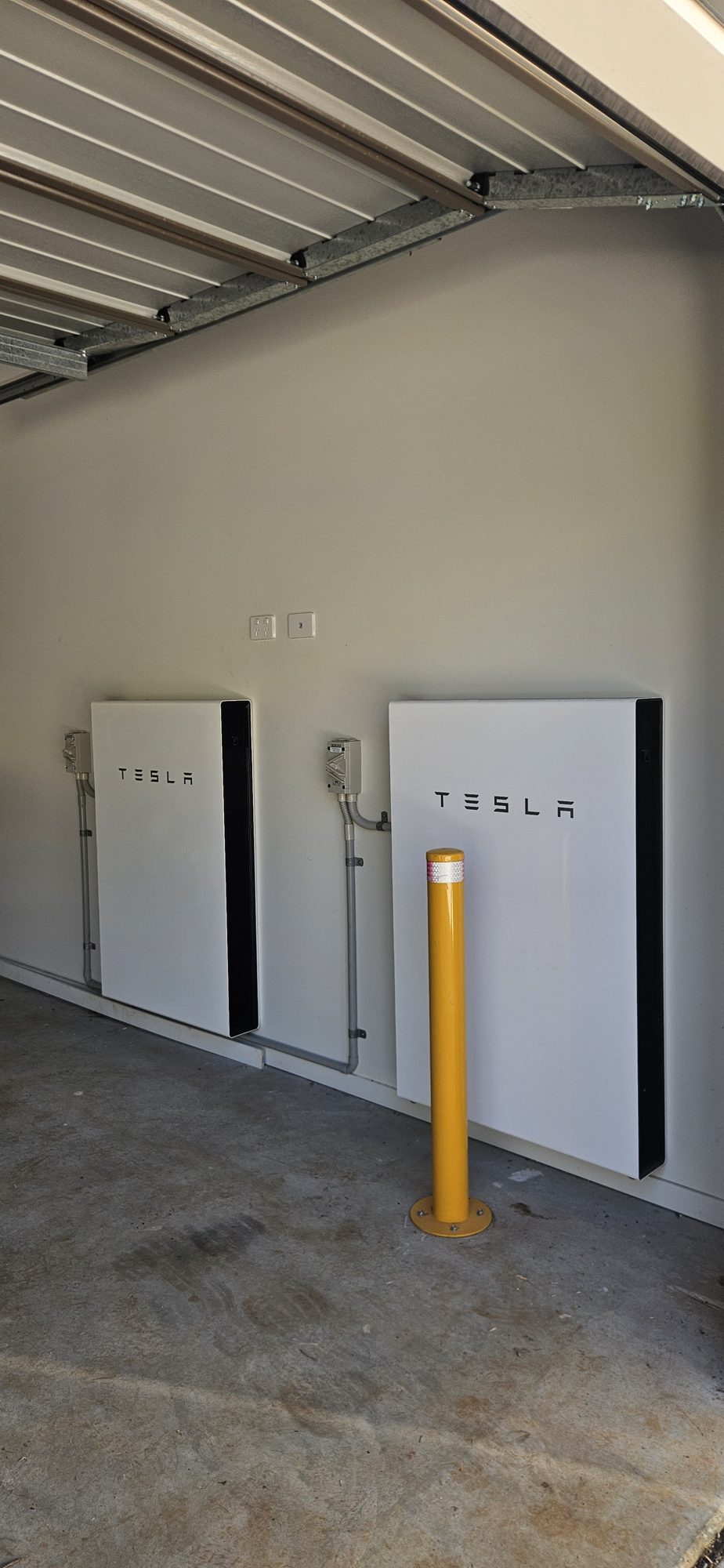 Two Tesla Powerwall batteries on a garage wall with a protective bollard, installed by Sun Connect Solar in the Northern Rivers