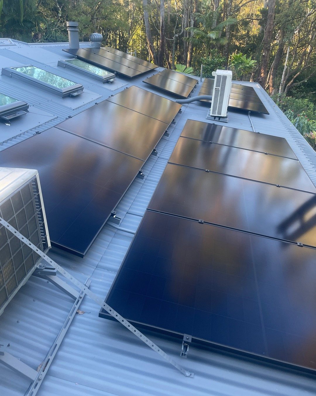 All-black AIKO solar panels on a grey metal roof at The Pocket, some on tilt frames, with forest behind, part of a solar and 16 kWh Sigenergy battery install by Sun Connect Solar