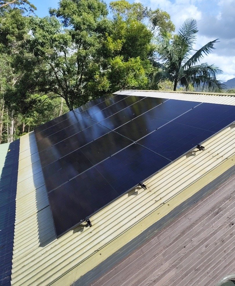 All-black AIKO solar panels on a metal roof with forest and palms behind at Upper Main Arm All-black AIKO solar panels on a metal roof with forest and palms behind at Upper Main Arm, installed by Sun Connect Solar