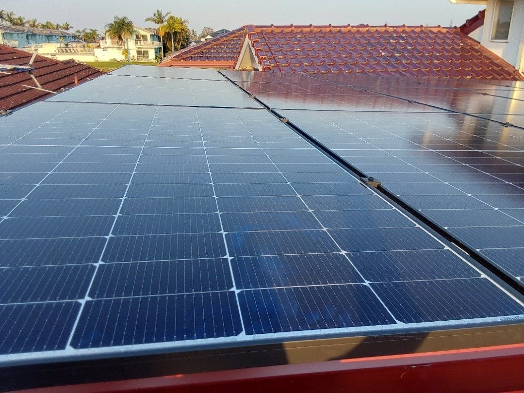 A Jinko solar array on a red tile roof with canal-side homes and palms behind in West Ballina A Jinko solar array on a red tile roof with canal-side homes and palms behind in West Ballina, installed by Sun Connect Solar