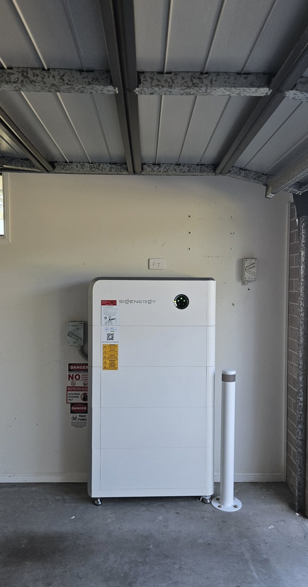 Three-phase Sigenergy SigenStor battery Three-phase Sigenergy SigenStor battery, about 32 kWh, in a garage with a steel bollard at a home in the Woodburn area, installed by Sun Connect Solar